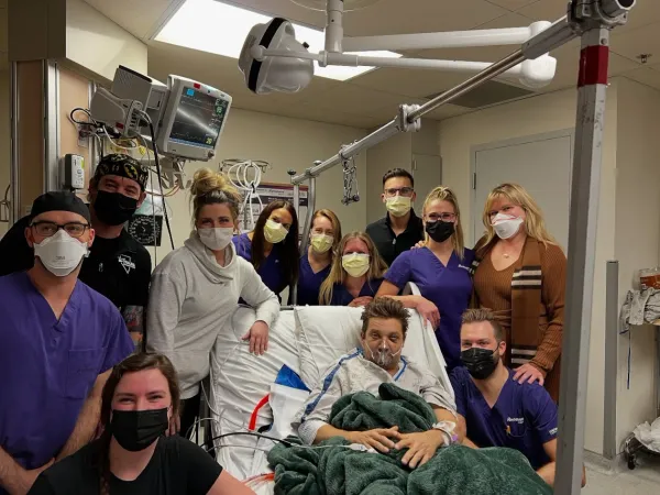  Jeremy Renner in hospital bed surrounded by medical team after snowplow accident.